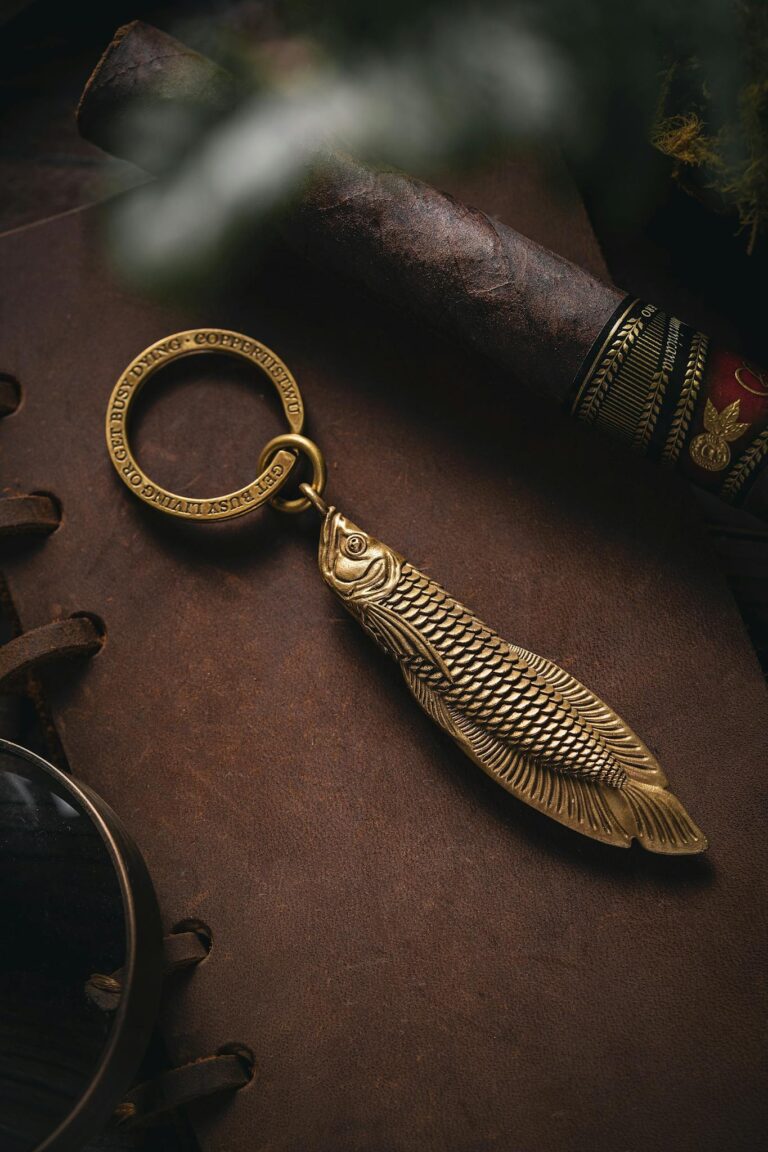 Close-up of a brass fish keychain elegantly resting on a leather journal, accompanied by a vintage cigar.